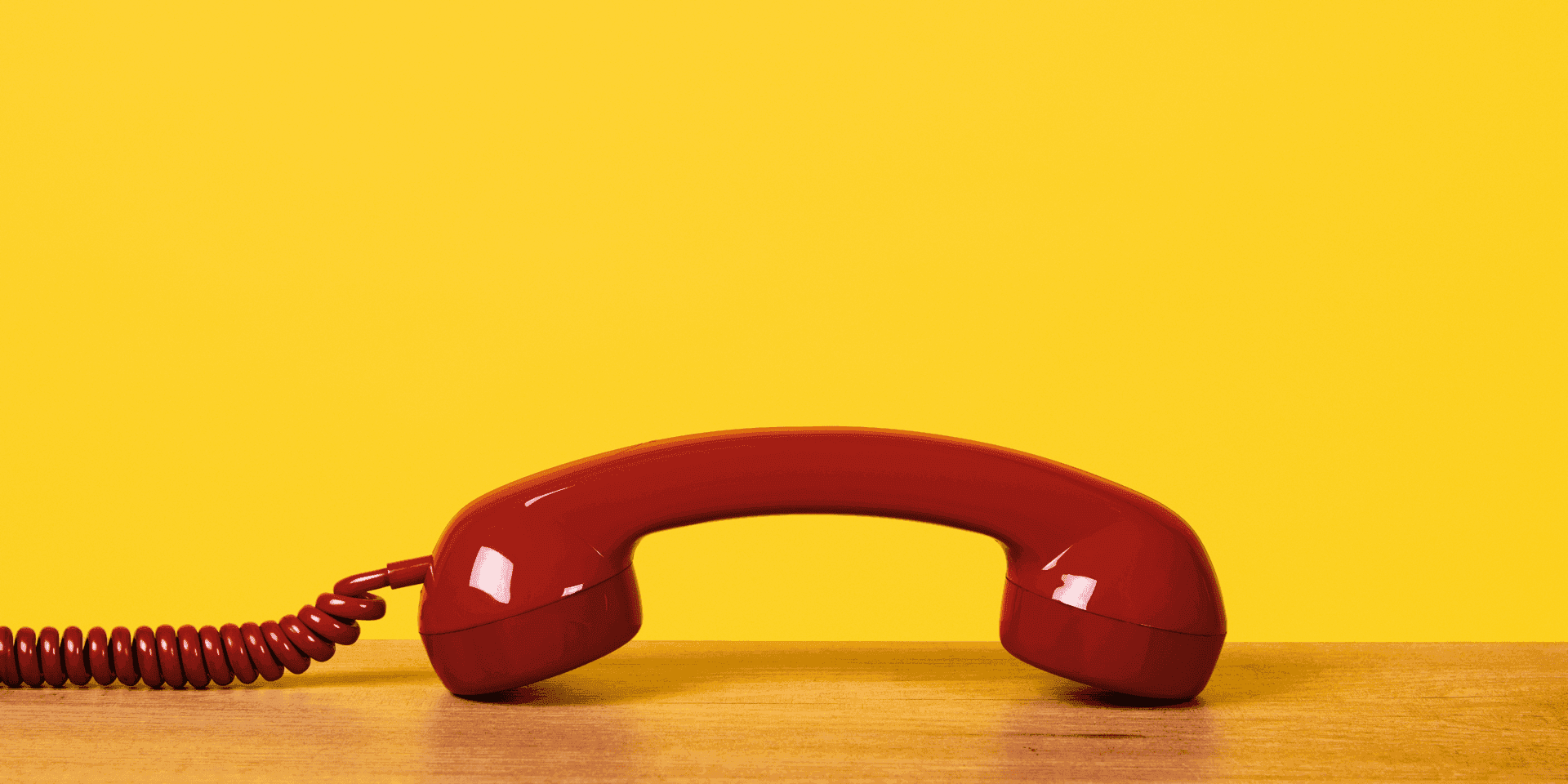 A classic red telephone handset resting on a wooden desk